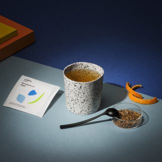 Cup of herbal infusion styled with colors geometric forms, orange zest and black spoon